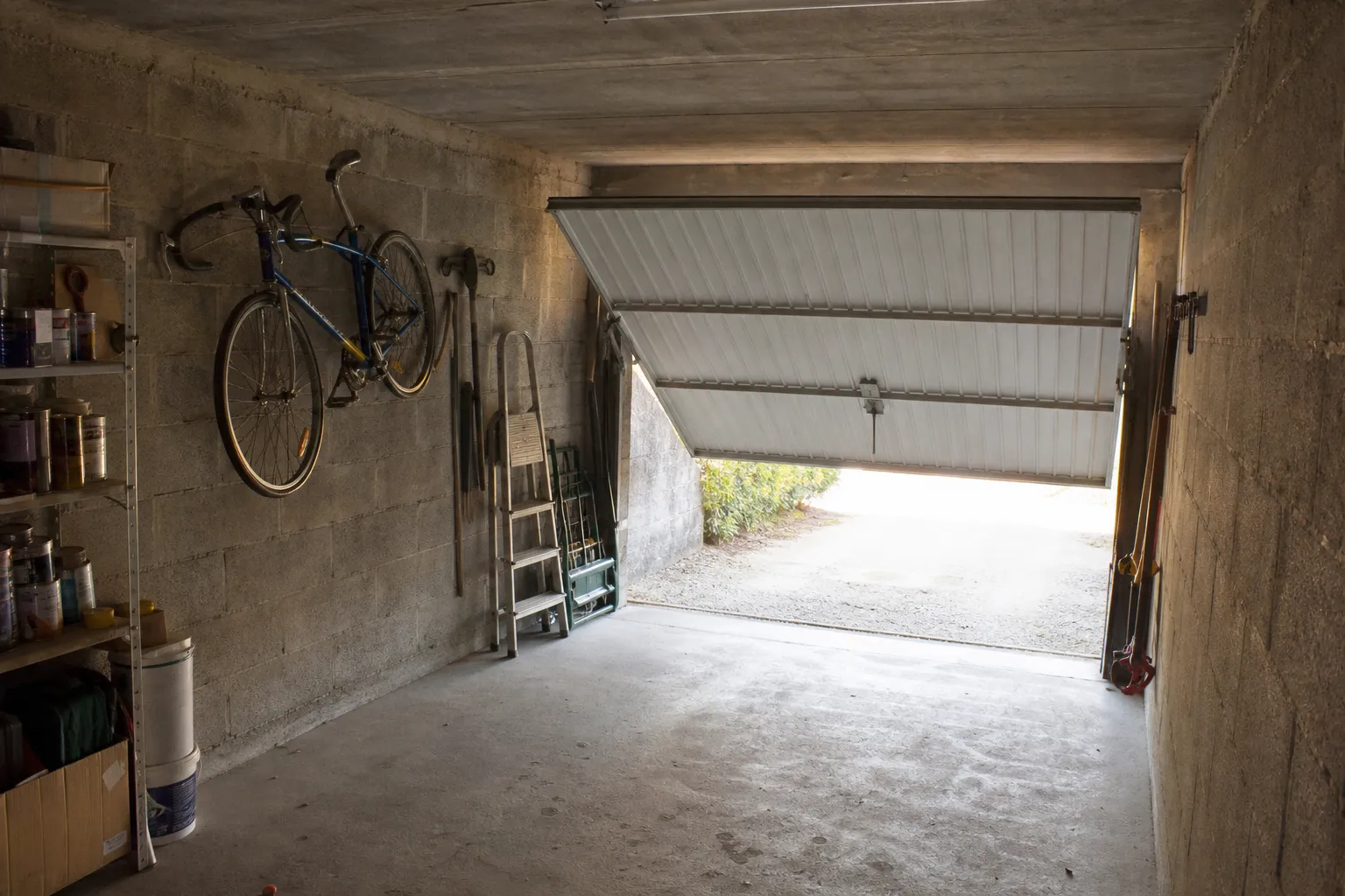 Intérieur d’un garage individuel en béton brut, porte basculante entrouverte sur la rue
